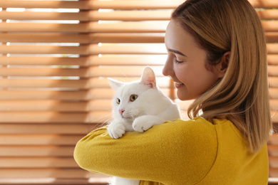 Young woman with her beautiful white cat near window at home. Fluffy pet