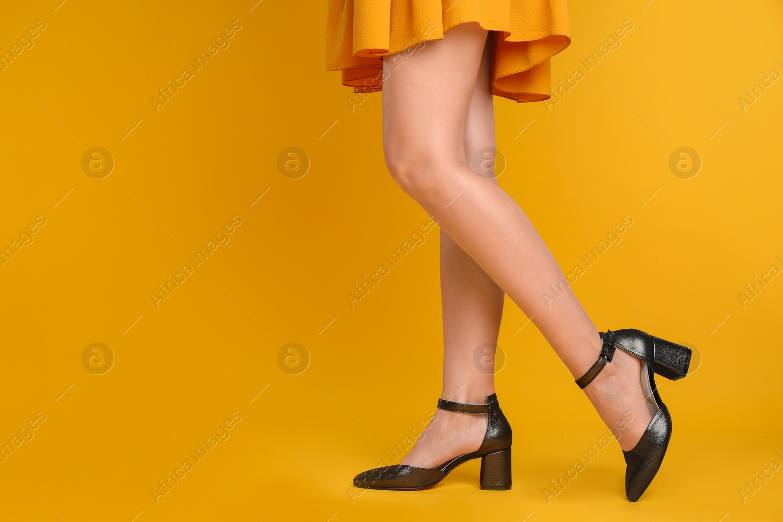 Photo of Woman wearing stylish shoes on yellow background, closeup. Space for text