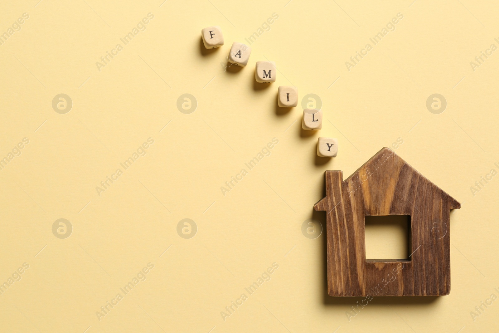 Photo of House figure and word Family made of cubes as smoke from chimney on pale yellow background, flat lay. Space for text