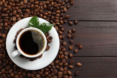 Photo of Cup of aromatic coffee and beans on wooden table, flat lay. Space for text