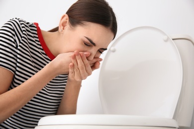 Photo of Young woman suffering from nausea at toilet bowl indoors