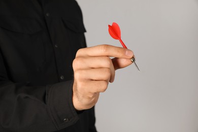 Man holding red dart on light background, closeup