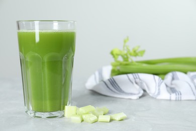 Glass of celery juice and fresh vegetables on light gray table