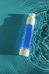 Photo of Bottle of cosmetic product in water on turquoise background, top view