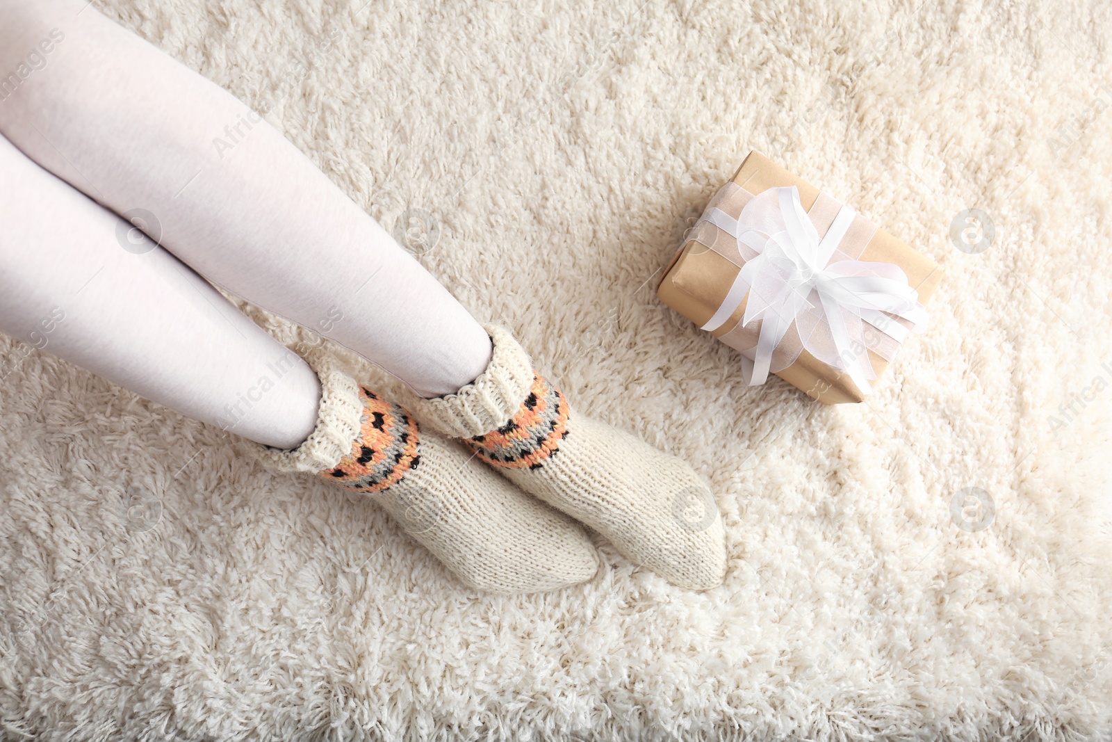 Photo of Woman wearing knitted socks on rug, top view. Warm clothes