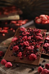Chocolate bars with different freeze dried fruits on wooden board, closeup