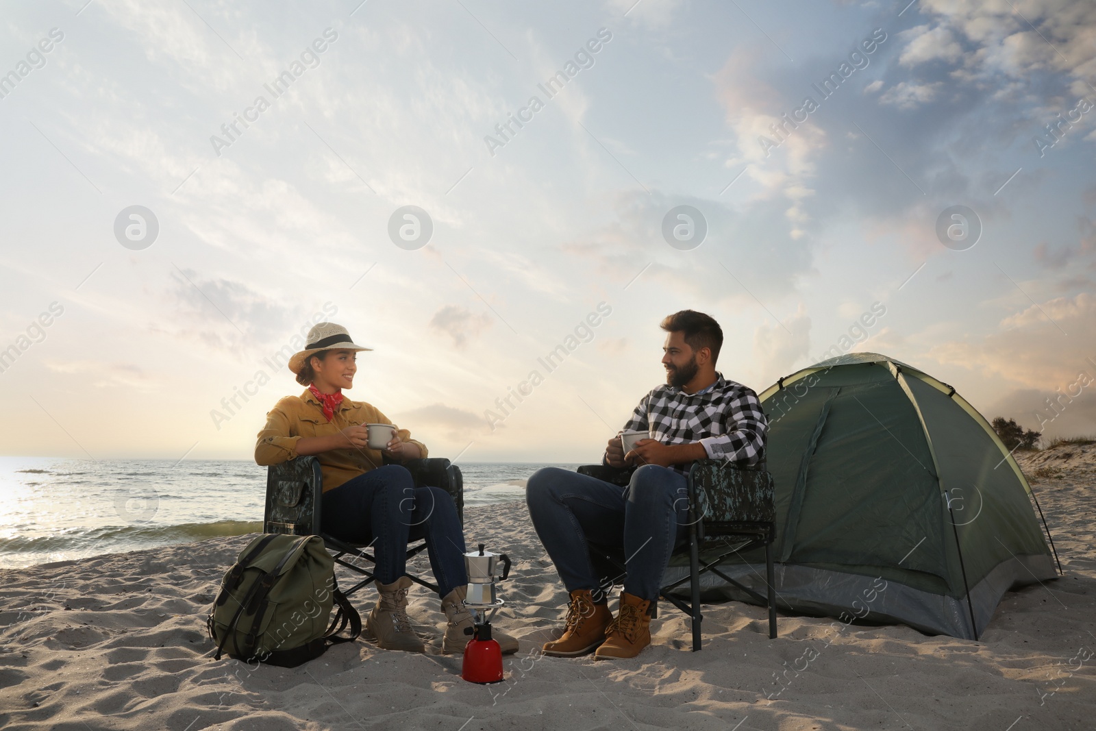 Photo of Couple with hot drinks near camping tent on beach