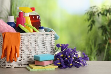 Spring cleaning. Plastic basket with detergents, supplies and beautiful flowers on wooden table outdoors, space for text