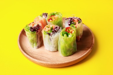 Photo of Different delicious spring rolls wrapped in rice paper on yellow background, closeup