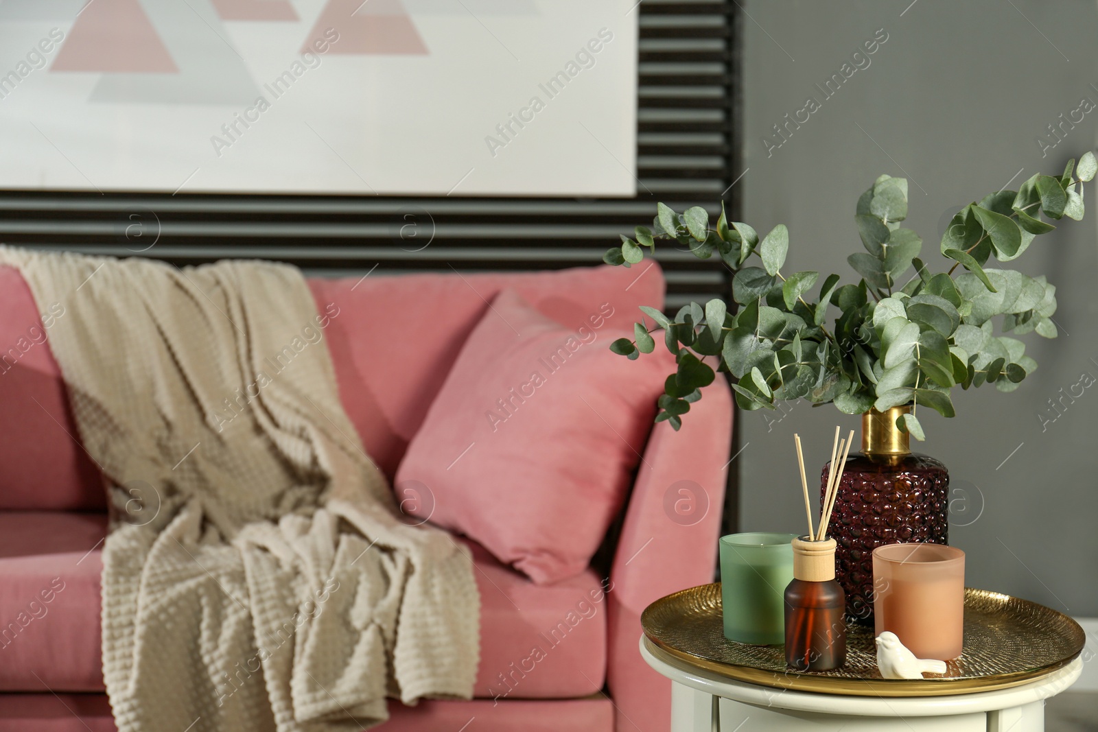 Photo of Eucalyptus branches, aromatic reed air freshener and candles on table in living room, space for text. Interior element