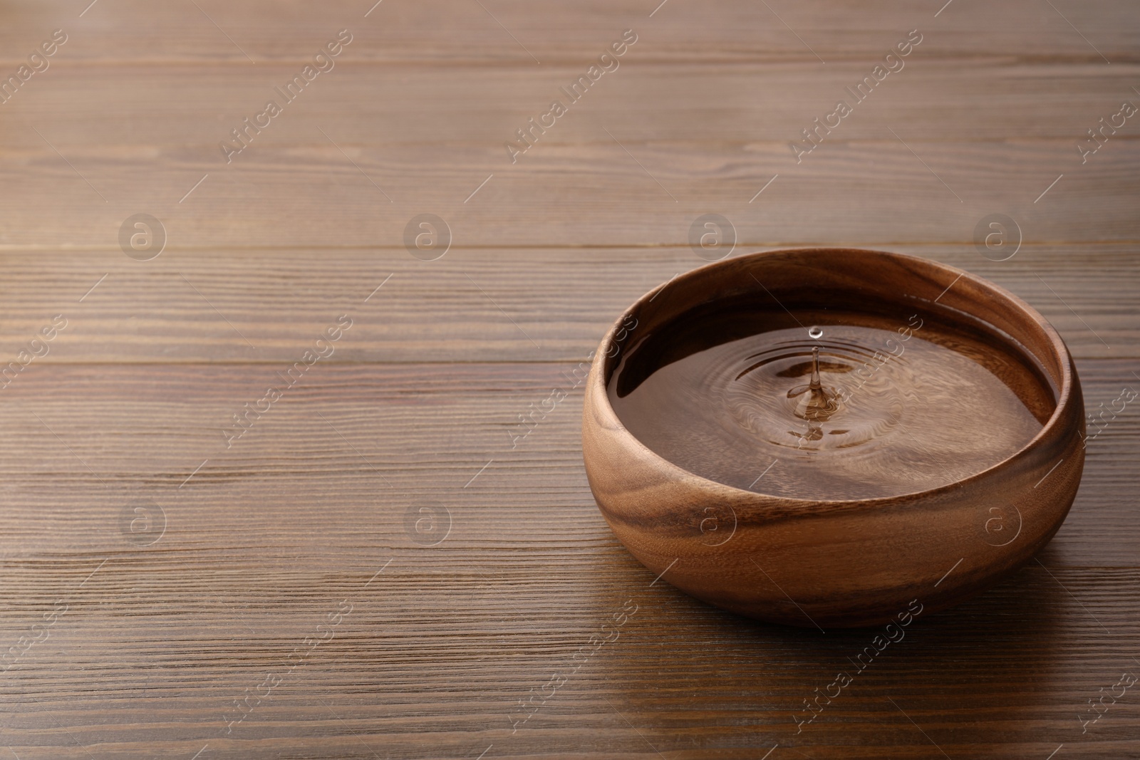 Photo of Drop falling down into bowl with clear water on wooden table. Space for text