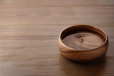Photo of Drop falling down into bowl with clear water on wooden table. Space for text