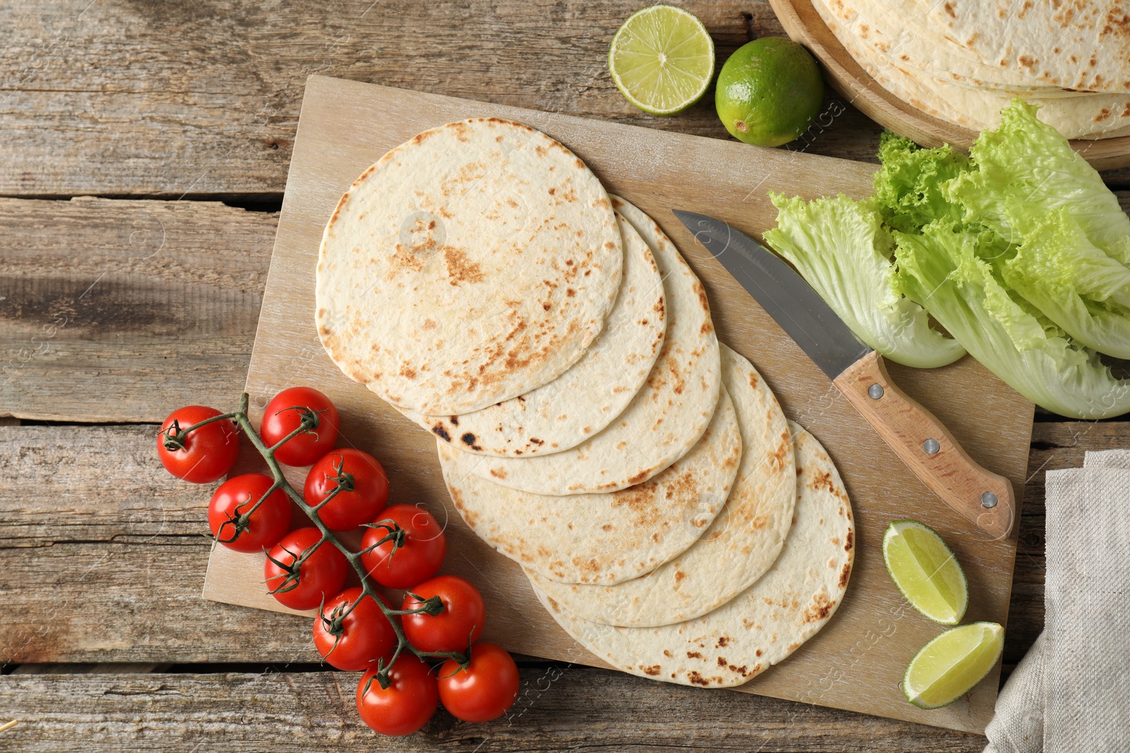 Photo of Tasty homemade tortillas, tomatoes, lime, lettuce and knife on wooden table, top view