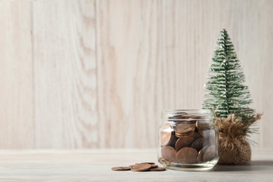 Photo of Glass jar with coins and small decorative tree on white wooden table. Space for text