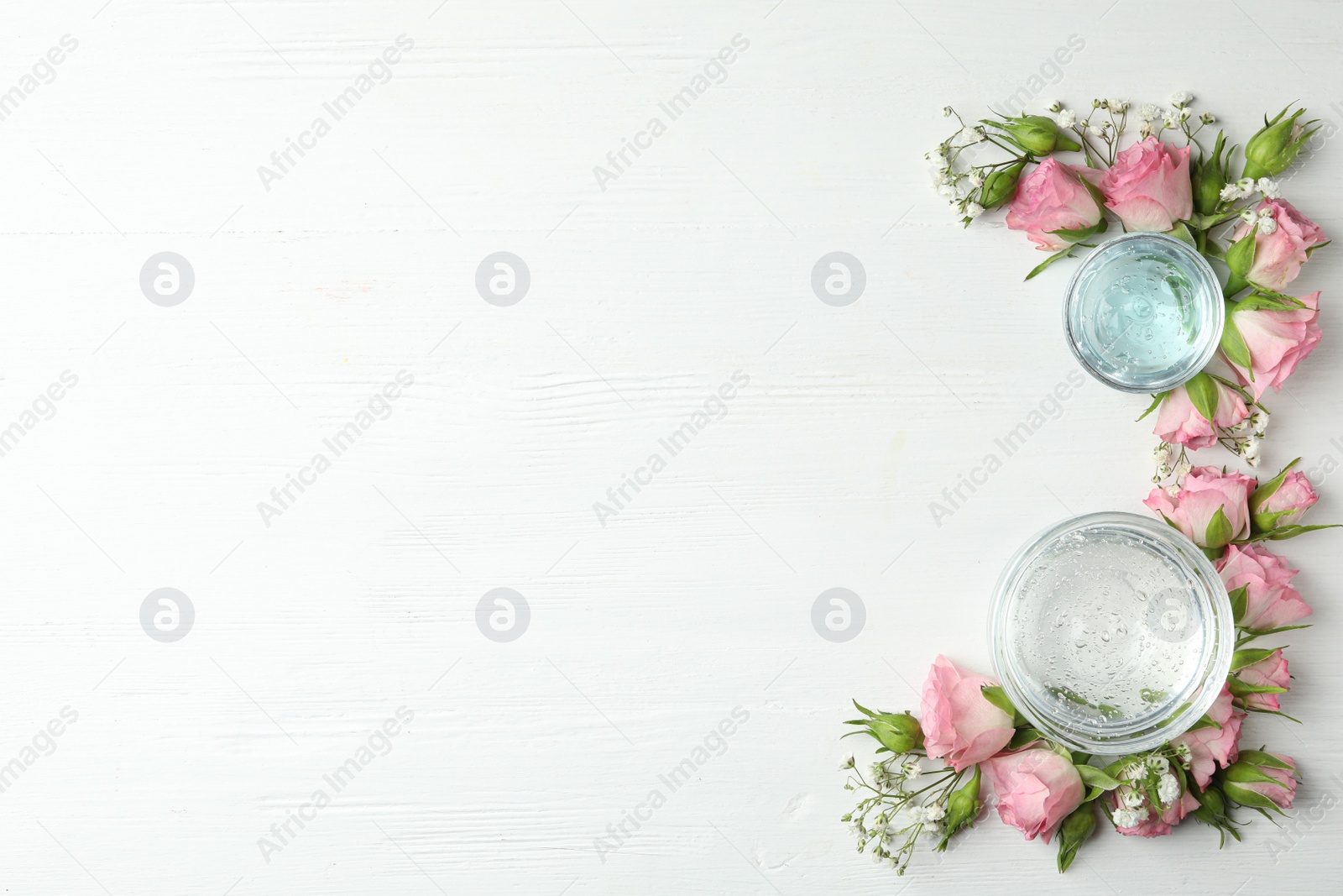 Photo of Flat lay composition with cosmetic gel and beautiful flowers on white wooden table. Space for text