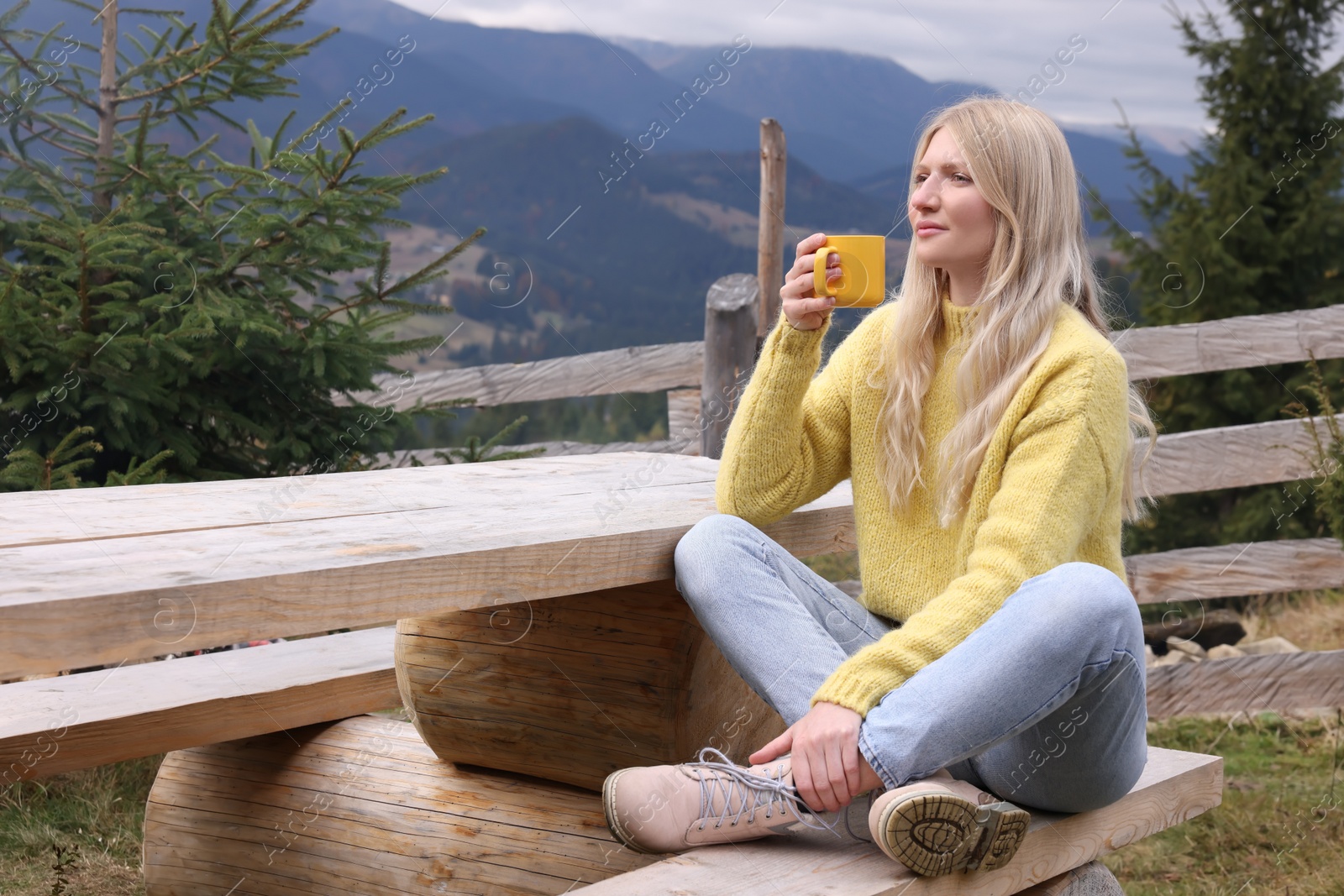 Photo of Young woman with mug of hot drink on wooden bench in mountains