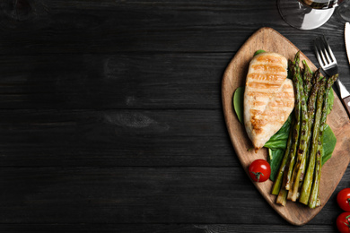 Photo of Tasty grilled chicken fillet served with asparagus on black wooden table, flat lay. Space for text