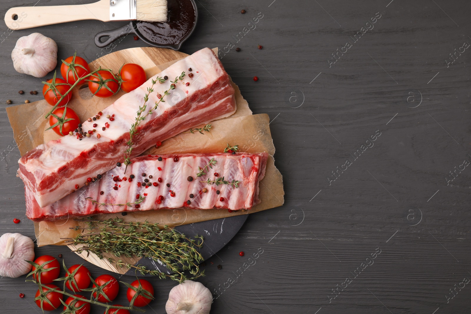Photo of Flat lay composition with raw pork ribs and spices on grey wooden table. Space for text