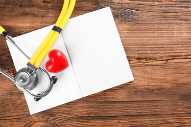 Photo of Stethoscope, open copybook and red heart on wooden background. Heart attack concept