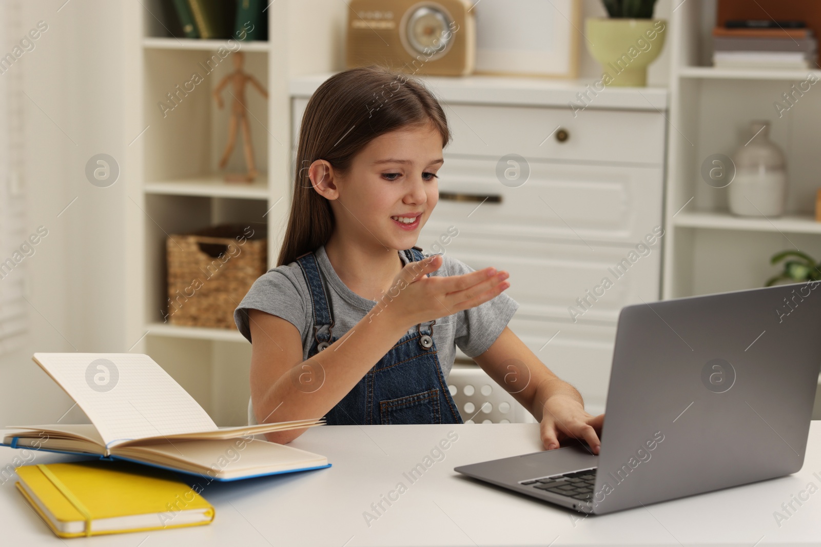 Photo of Cute girl using laptop at white table indoors