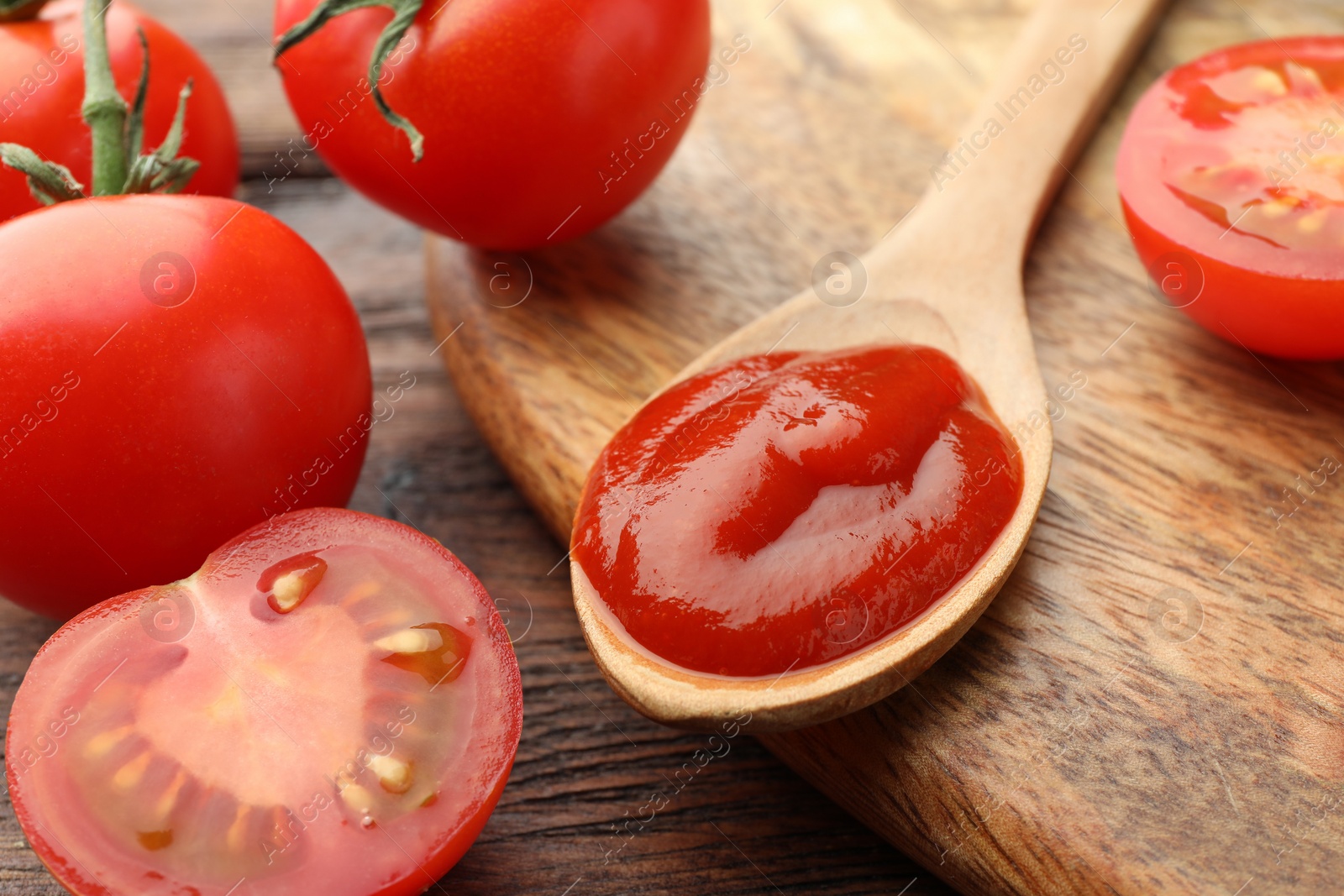 Photo of Spoon of tasty ketchup and tomatoes on wooden table, closeup