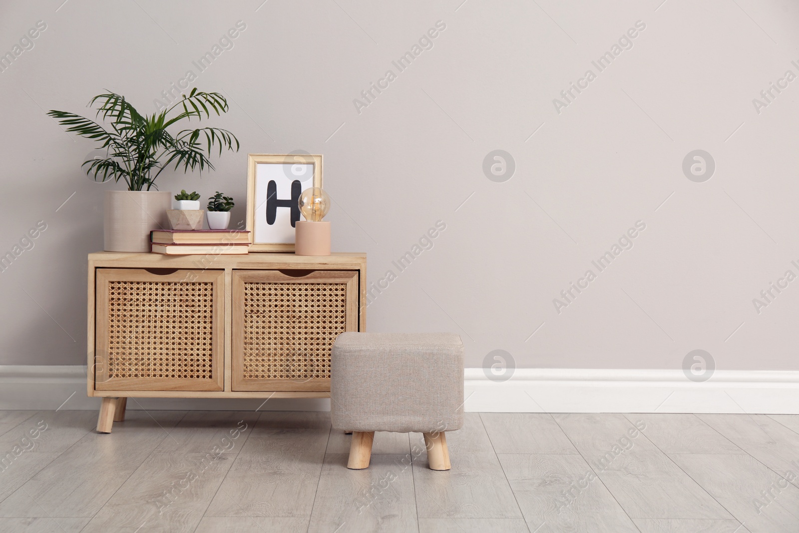 Photo of Stylish pouf and cabinet near beige wall indoors. Space for text