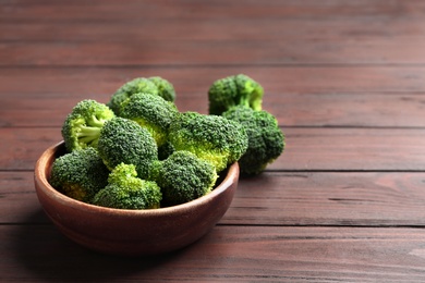 Photo of Bowl of fresh green broccoli on wooden table, space for text