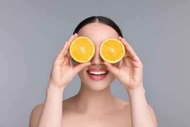 Beautiful young woman covering face with pieces of orange on grey background