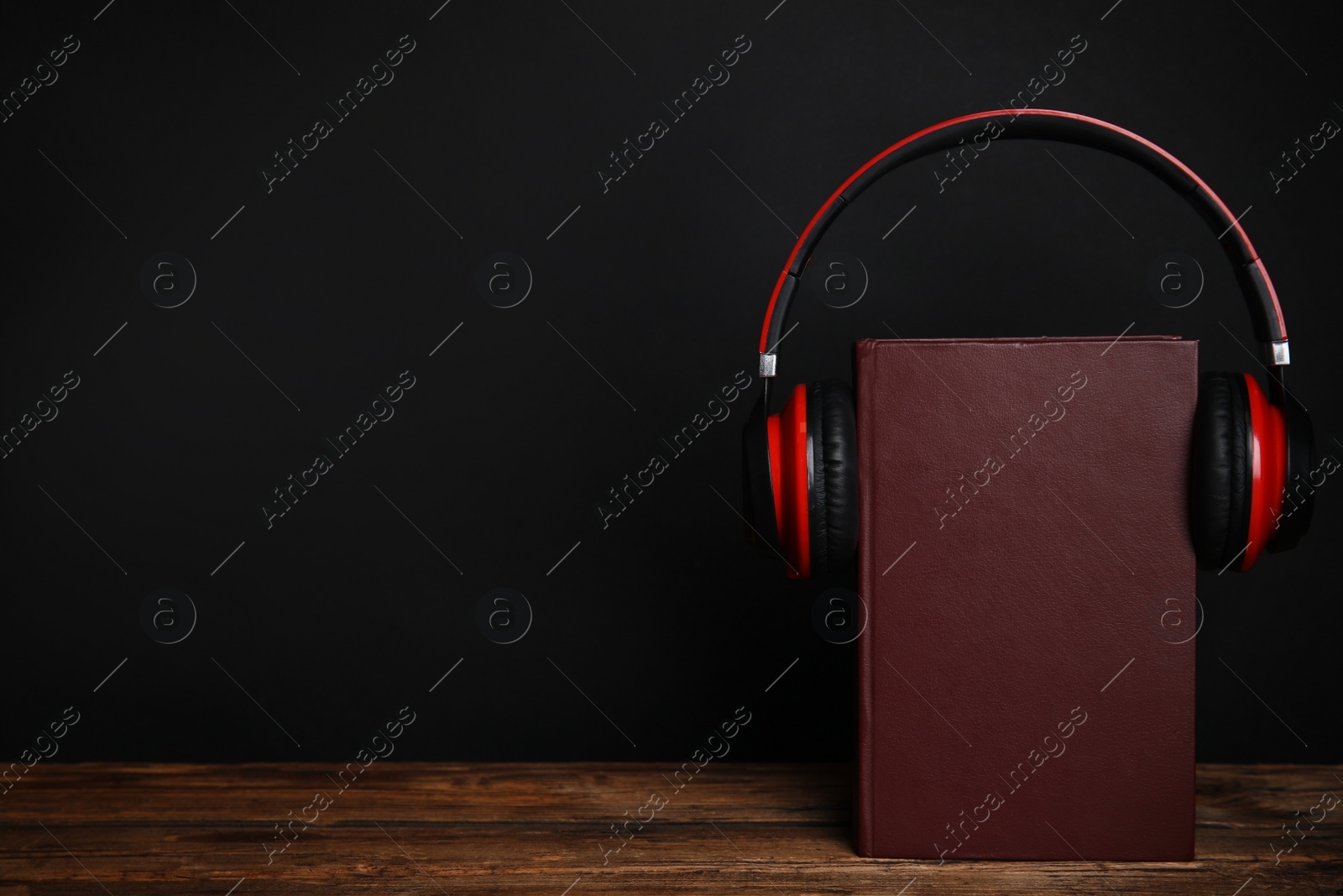 Photo of Book and modern headphones on wooden table against black background. Space for text