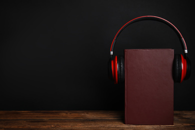 Photo of Book and modern headphones on wooden table against black background. Space for text