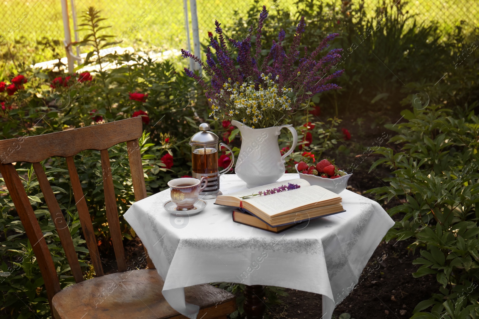 Photo of Beautiful bouquet of wildflowers and books on table served for tea drinking in garden