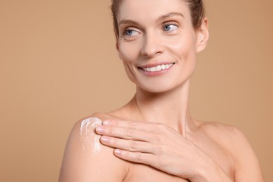 Woman applying body cream onto her arm against beige background, closeup. Space for text