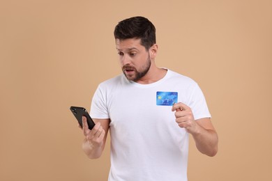 Photo of Emotional man with credit card and smartphone on beige background. Be careful - fraud