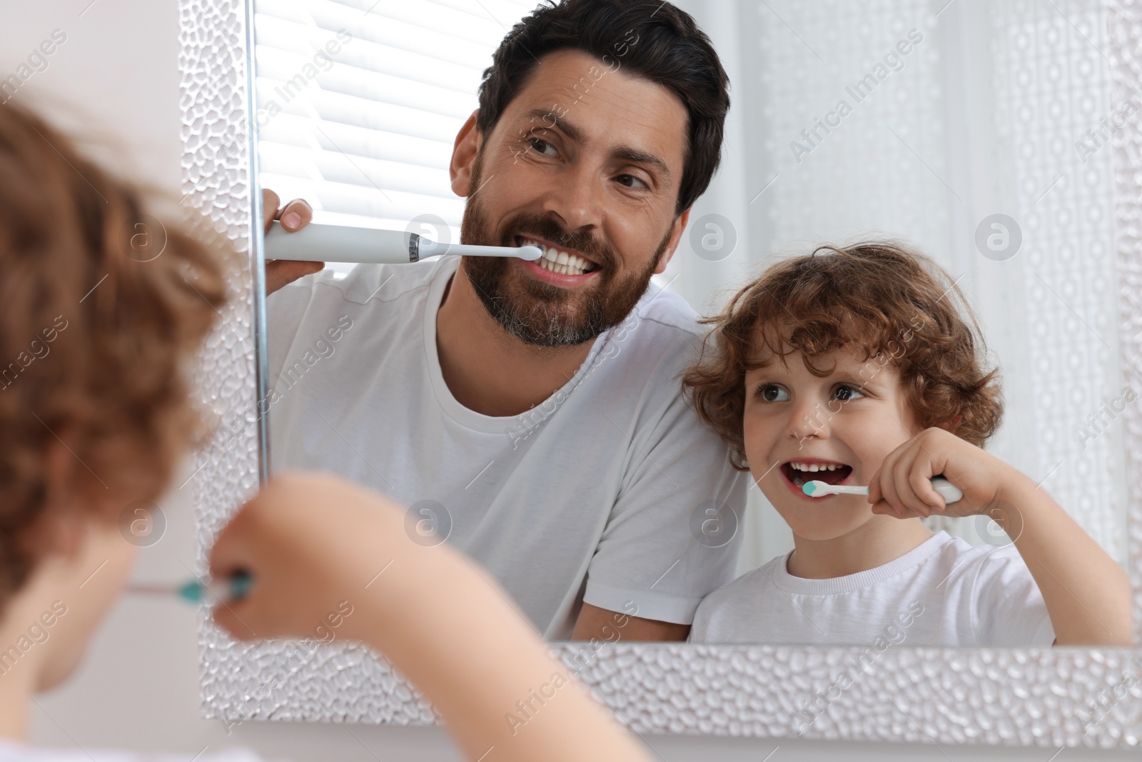 Photo of Father and his son brushing teeth together near mirror in bathroom