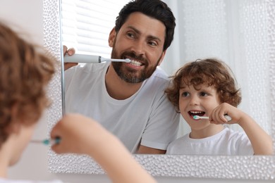 Photo of Father and his son brushing teeth together near mirror in bathroom