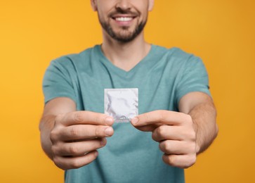 Happy man holding condom on orange background, closeup