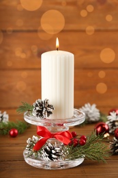 Glass candlestick with burning candle and Christmas decor on wooden table