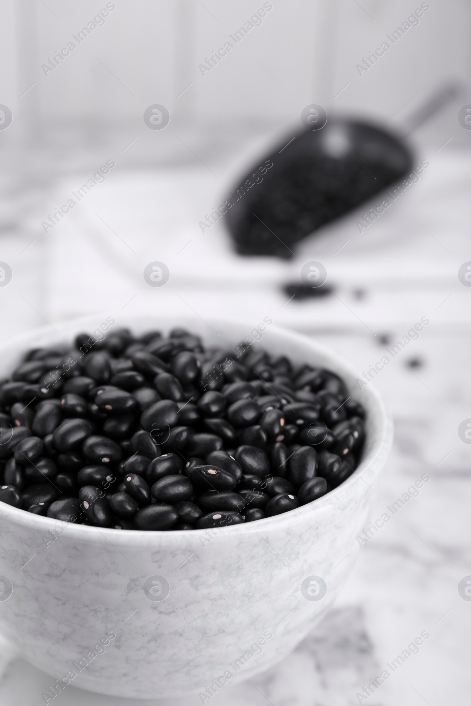 Photo of Bowl of raw black beans on white marble table, closeup
