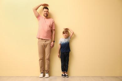 Father and son comparing their heights near beige wall indoors. Space for text