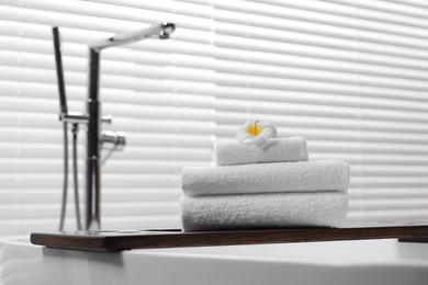 Photo of Stacked bath towels and beautiful flower on tub tray in bathroom