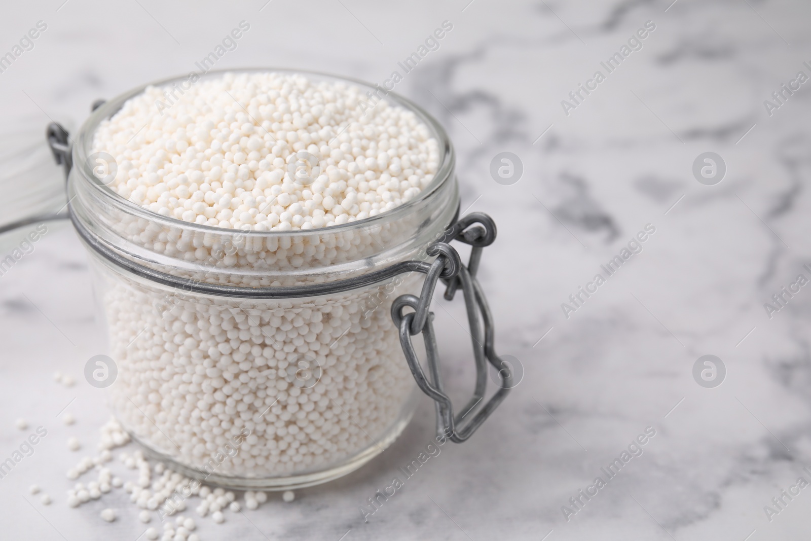 Photo of Tapioca pearls in jar on white marble table, closeup. Space for text