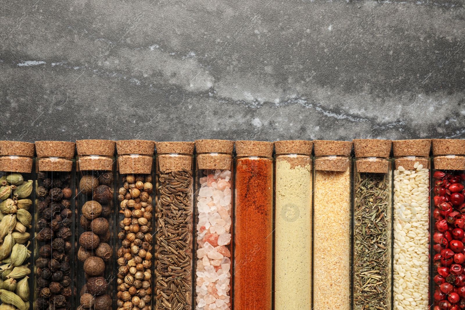 Photo of Glass tubes with different spices on grey marble table, flat lay. Space for text