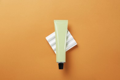 Tube of hand cream on orange background, top view