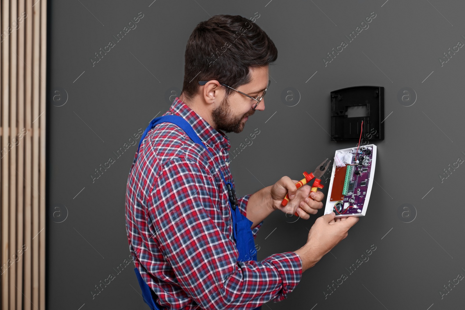 Photo of Technician installing home security alarm system on gray wall indoors