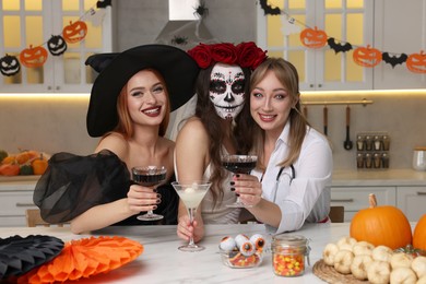 Group of women in scary costumes with cocktails celebrating Halloween indoors