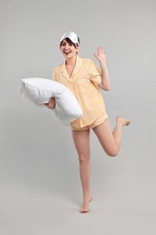 Photo of Happy woman in pyjama and sleep mask holding pillow on grey background