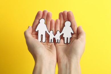 Woman holding paper family cutout on yellow  background, closeup