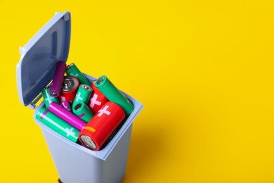 Many used batteries in recycling bin on yellow background, closeup. Space for text