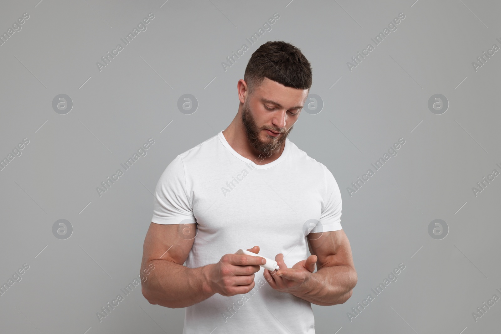 Photo of Handsome man applying body cream on light grey background
