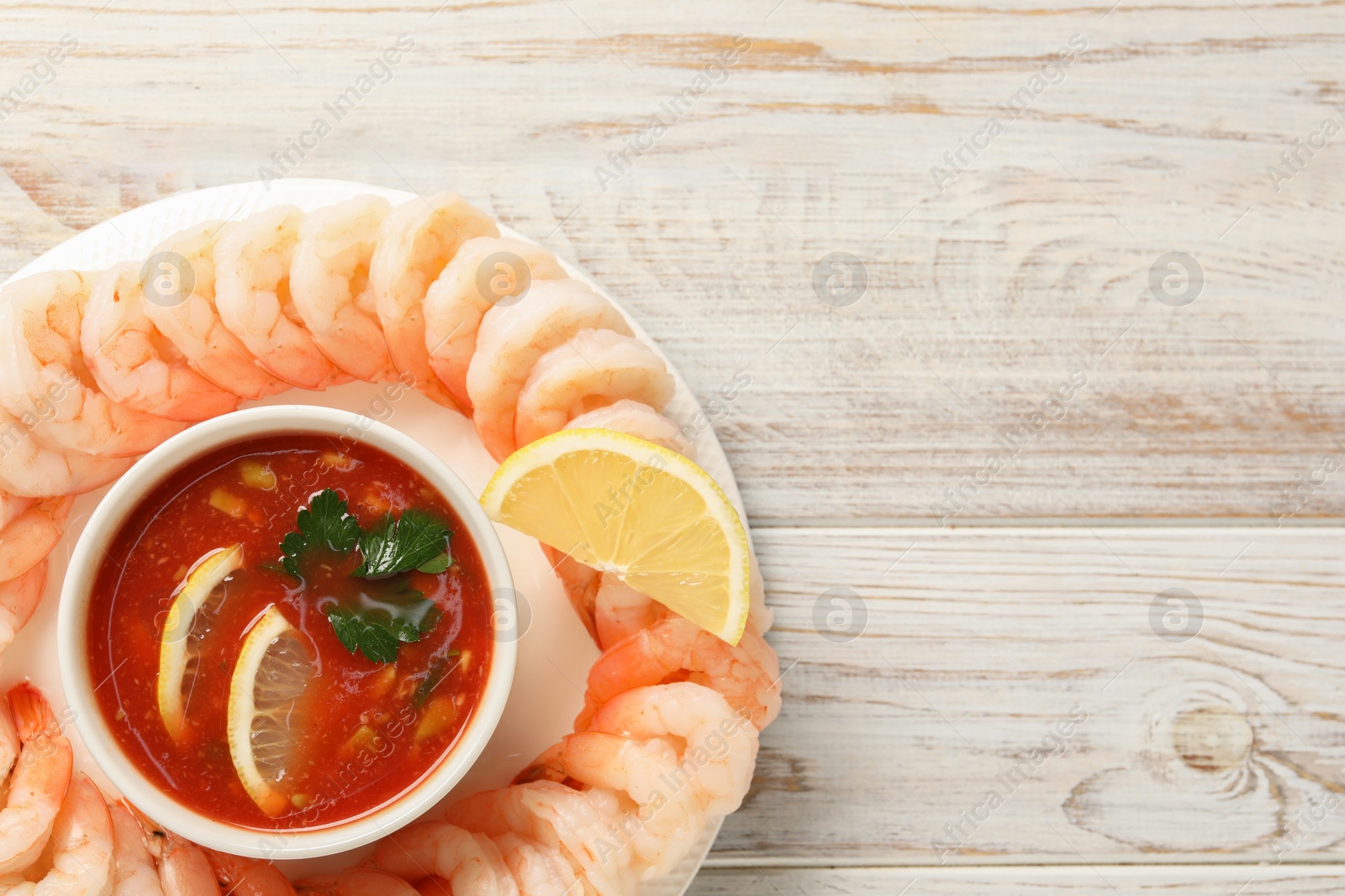 Photo of Tasty boiled shrimps with cocktail sauce and lemon on white wooden table, top view. Space for text